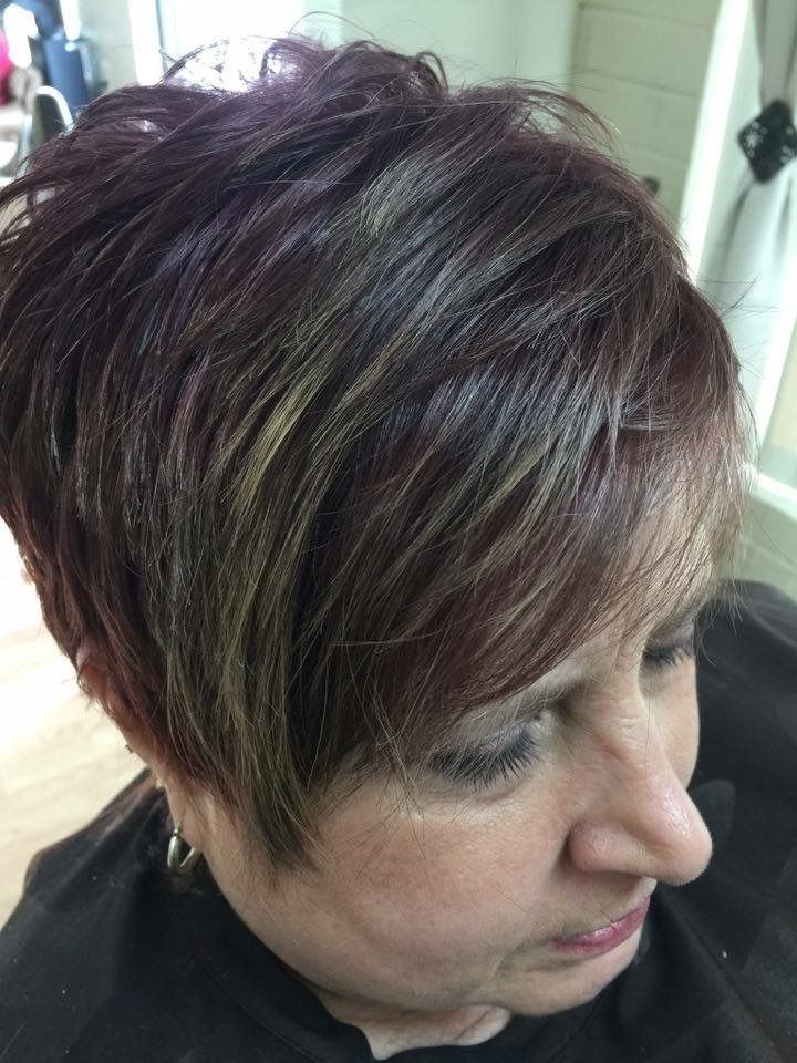 Close-up of a person with short dark hair and blonde highlights, looking downward in a salon chair.