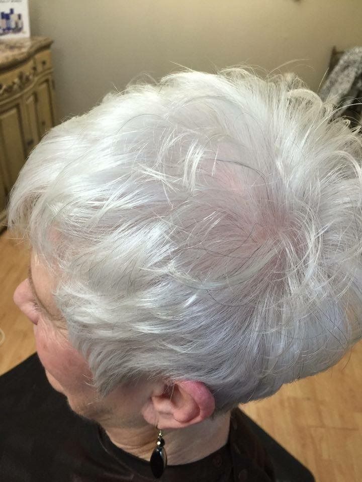 Side view of a person with short white hair indoors, wearing a black earring.