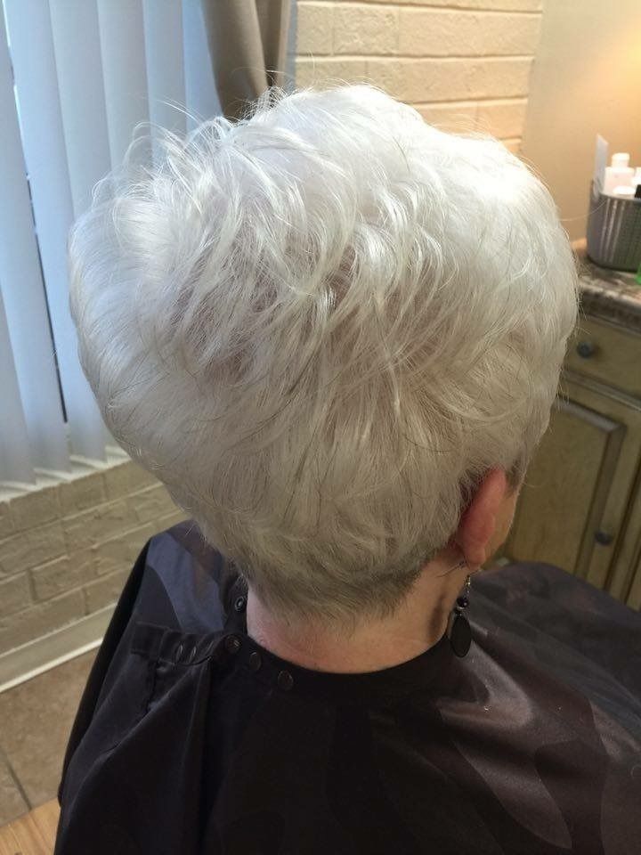 Short white pixie haircut viewed from the back in a salon chair, with layered volume at the crown.