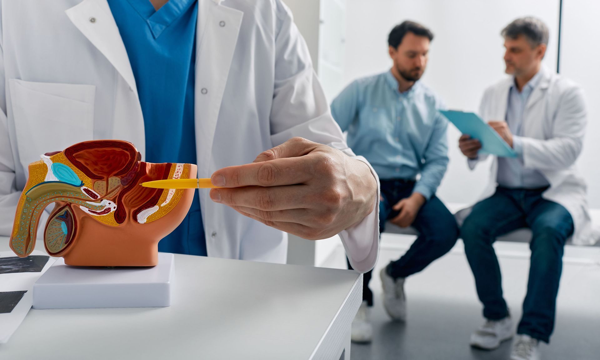 Médico apontando para um modelo anatômico da orelha em uma clínica enquanto dois homens desfocados conversam ao fundo.