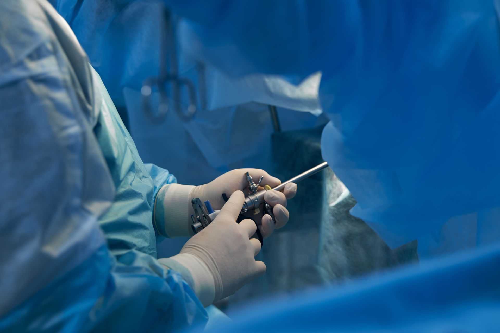 Cirurgiões com jalecos e luvas azuis operando um instrumento médico em uma sala de cirurgia estéril.