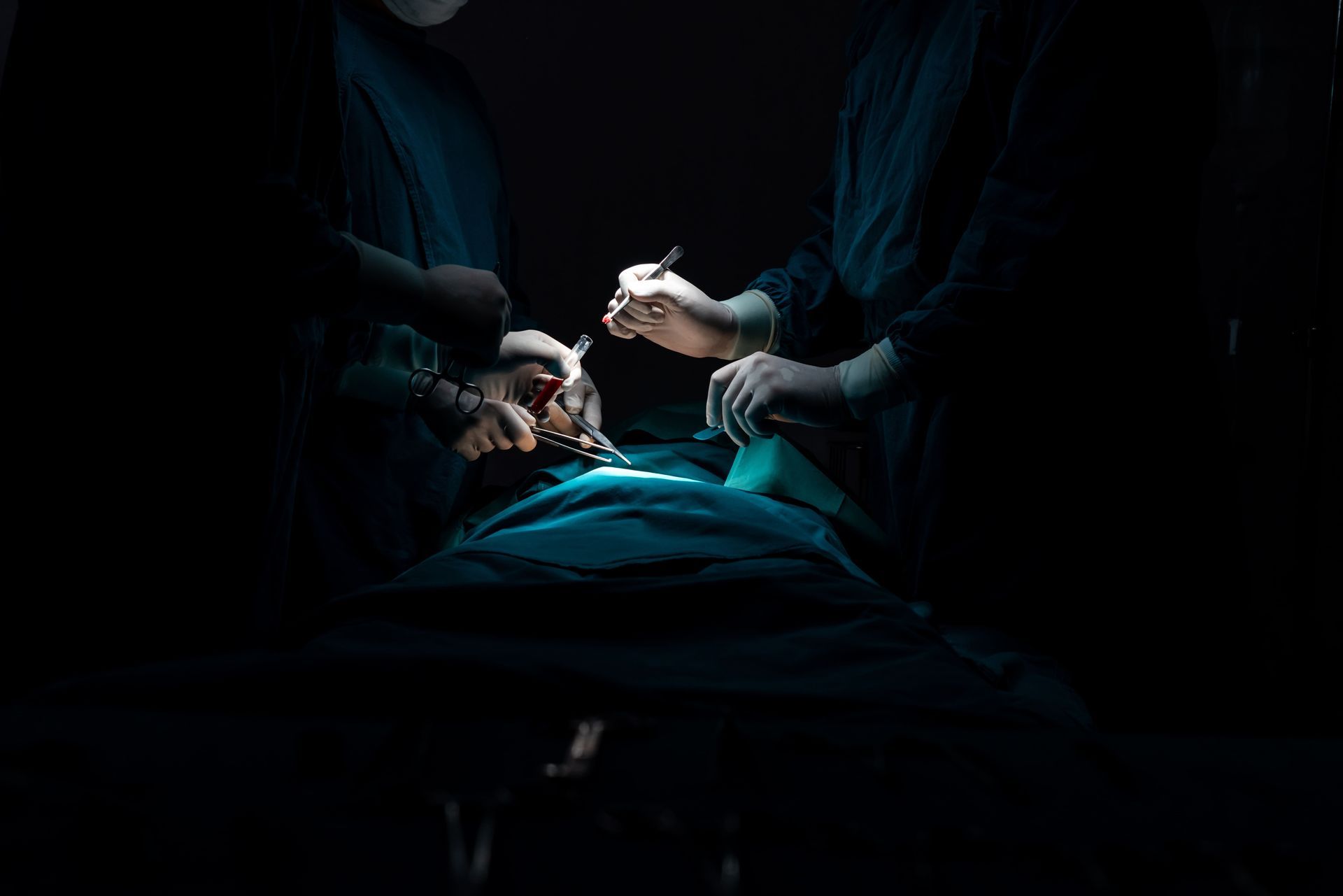 Equipe médica realizando um procedimento em um paciente sob iluminação cirúrgica azul fraca.