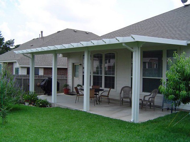 Back patio with white columns, chairs, and a green lawn beside a house