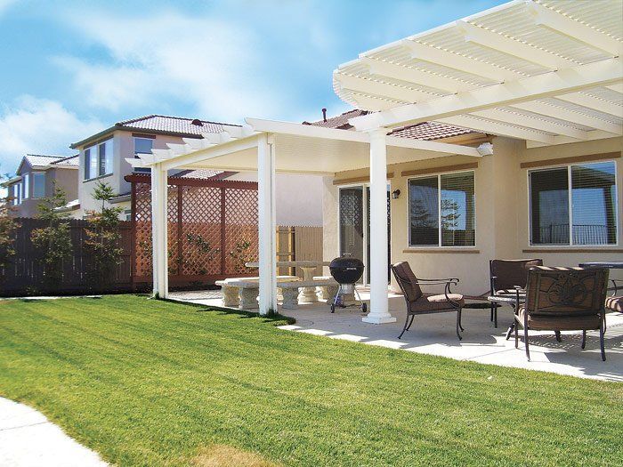 Backyard patio with white pergola, outdoor seating, and green lawn beside a house