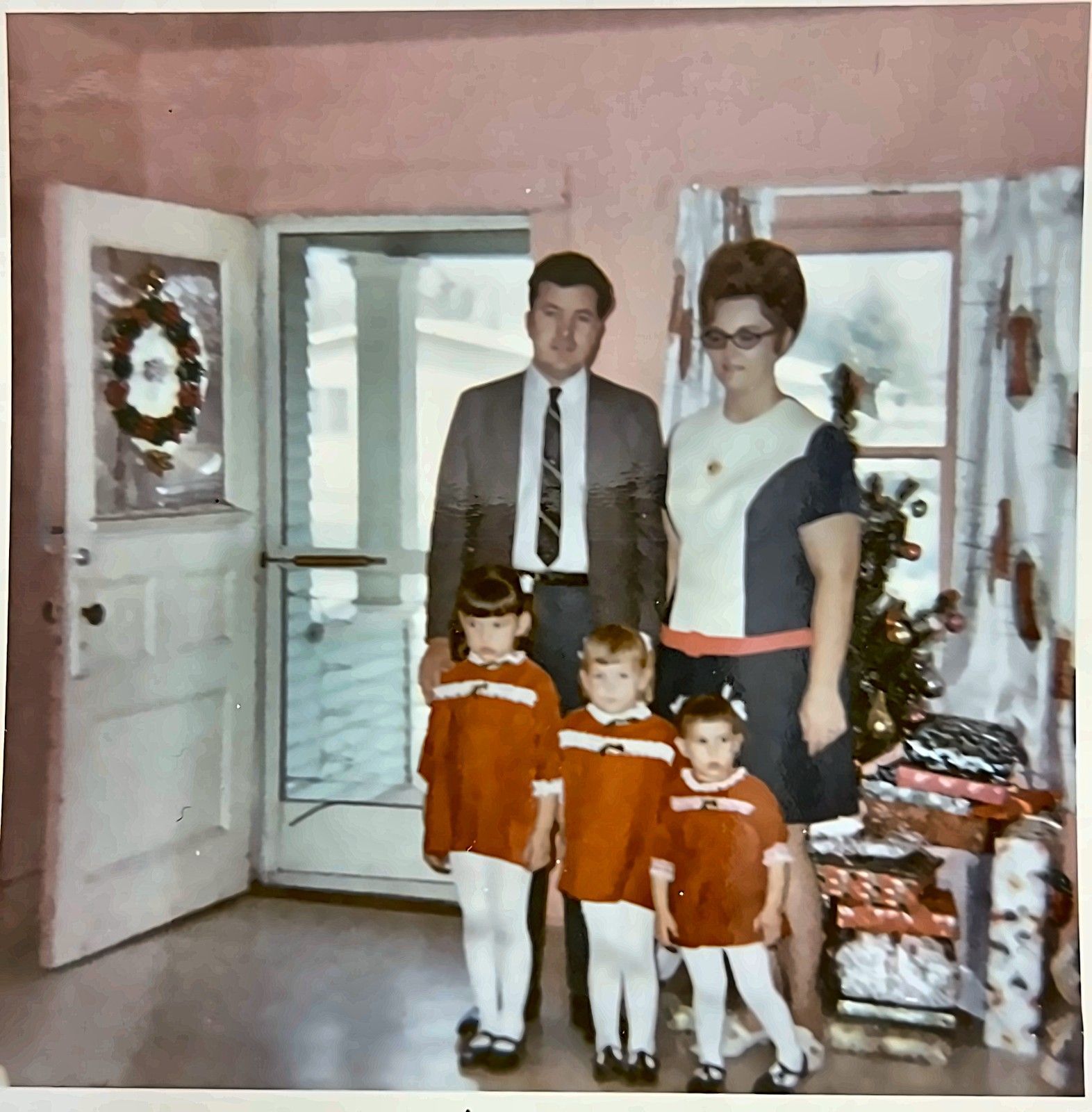 Family posing in a living room beside wrapped gifts, with a man, woman, and three children in matching outfits.
