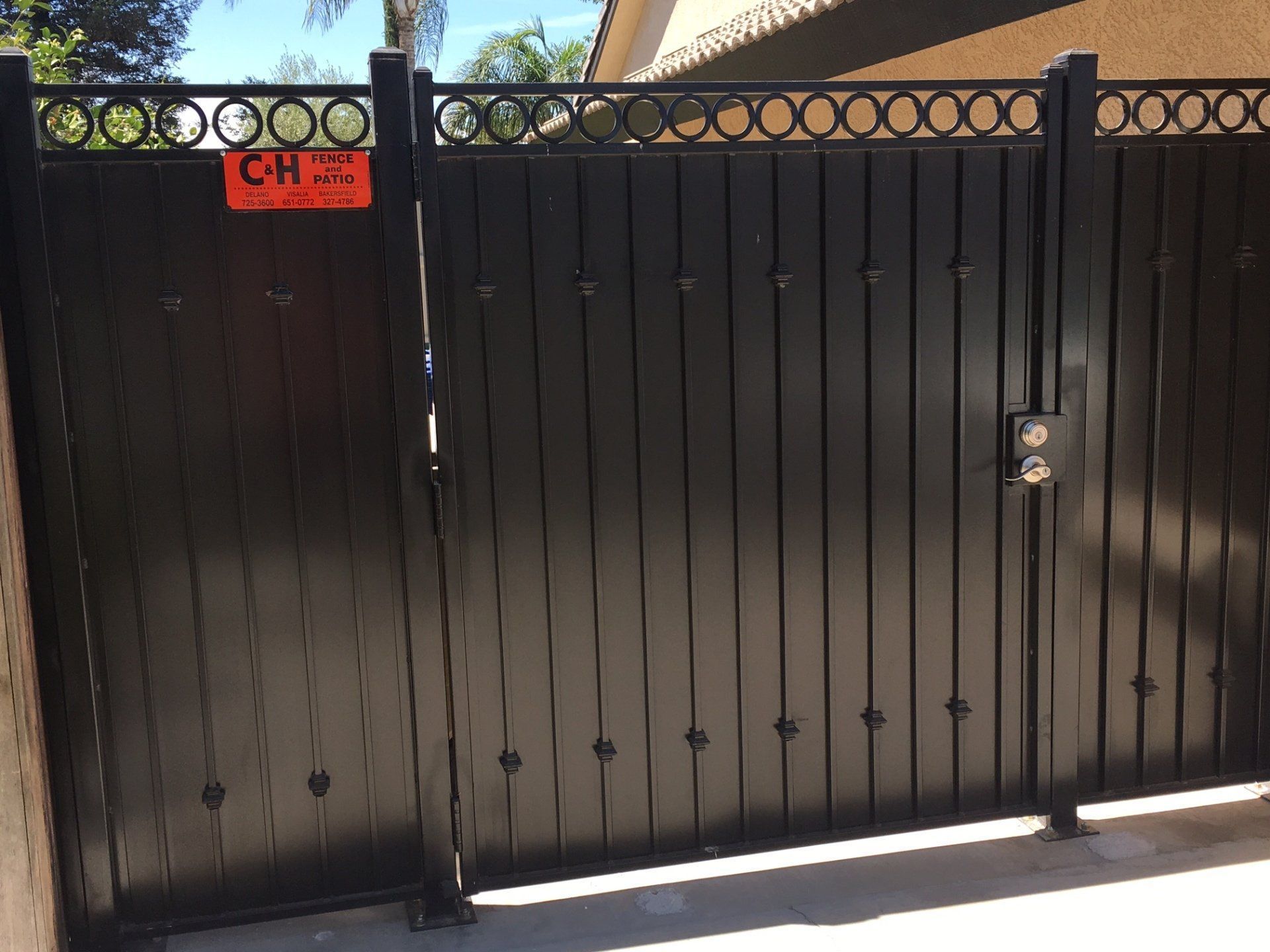 Black metal driveway gate with a small red sign and round decorative circles along the top