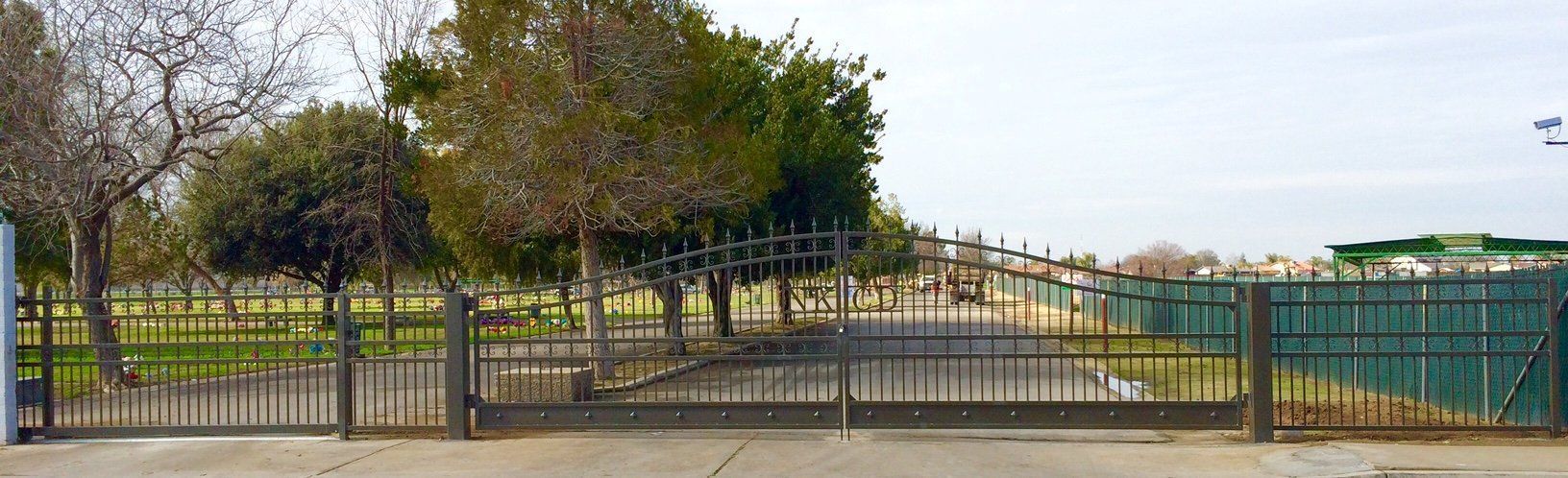 Gated entrance to a park with trees and a paved path under a clear sky