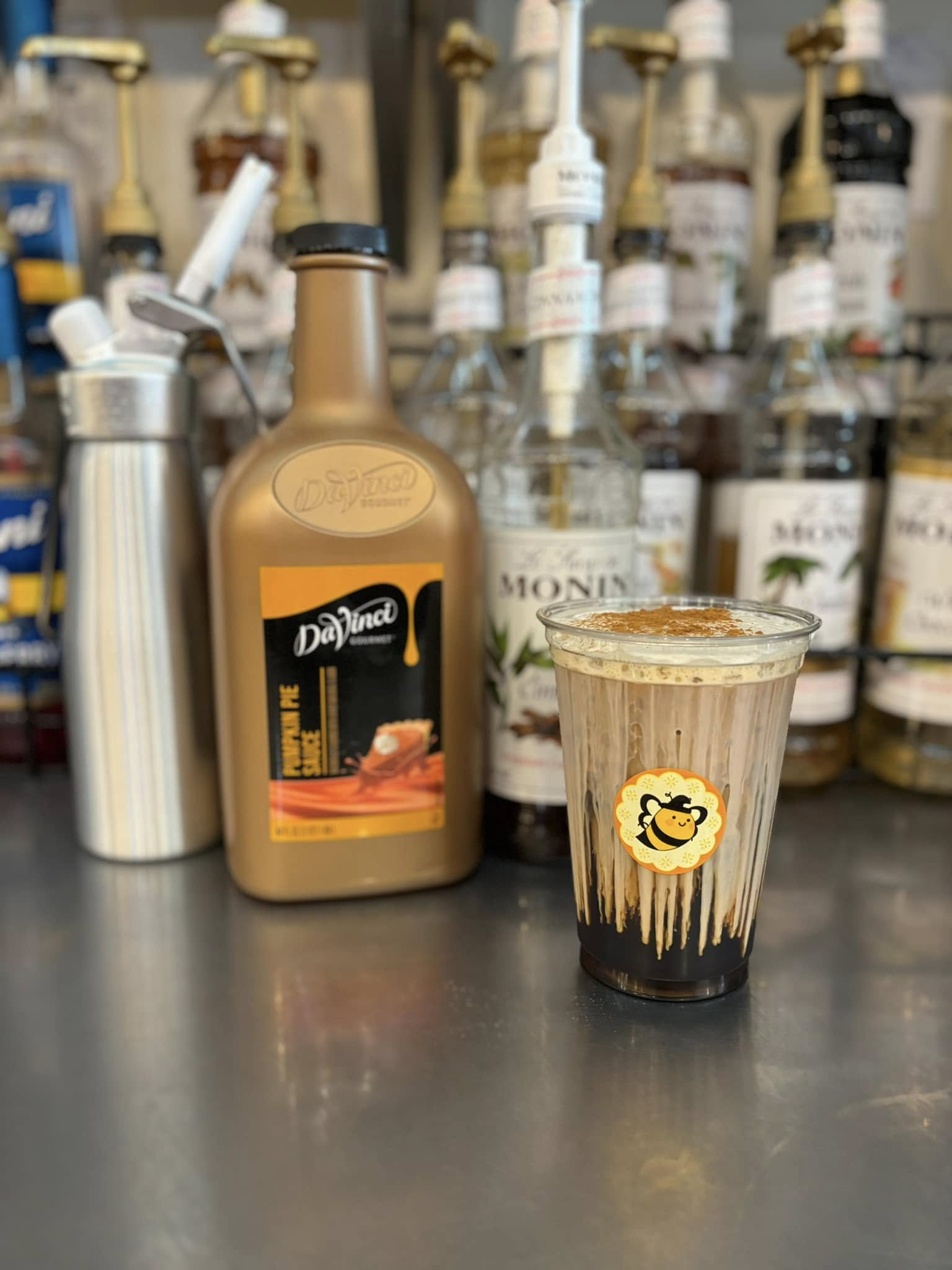 A cup of beverage with syrup bottles and dispenser on a counter.