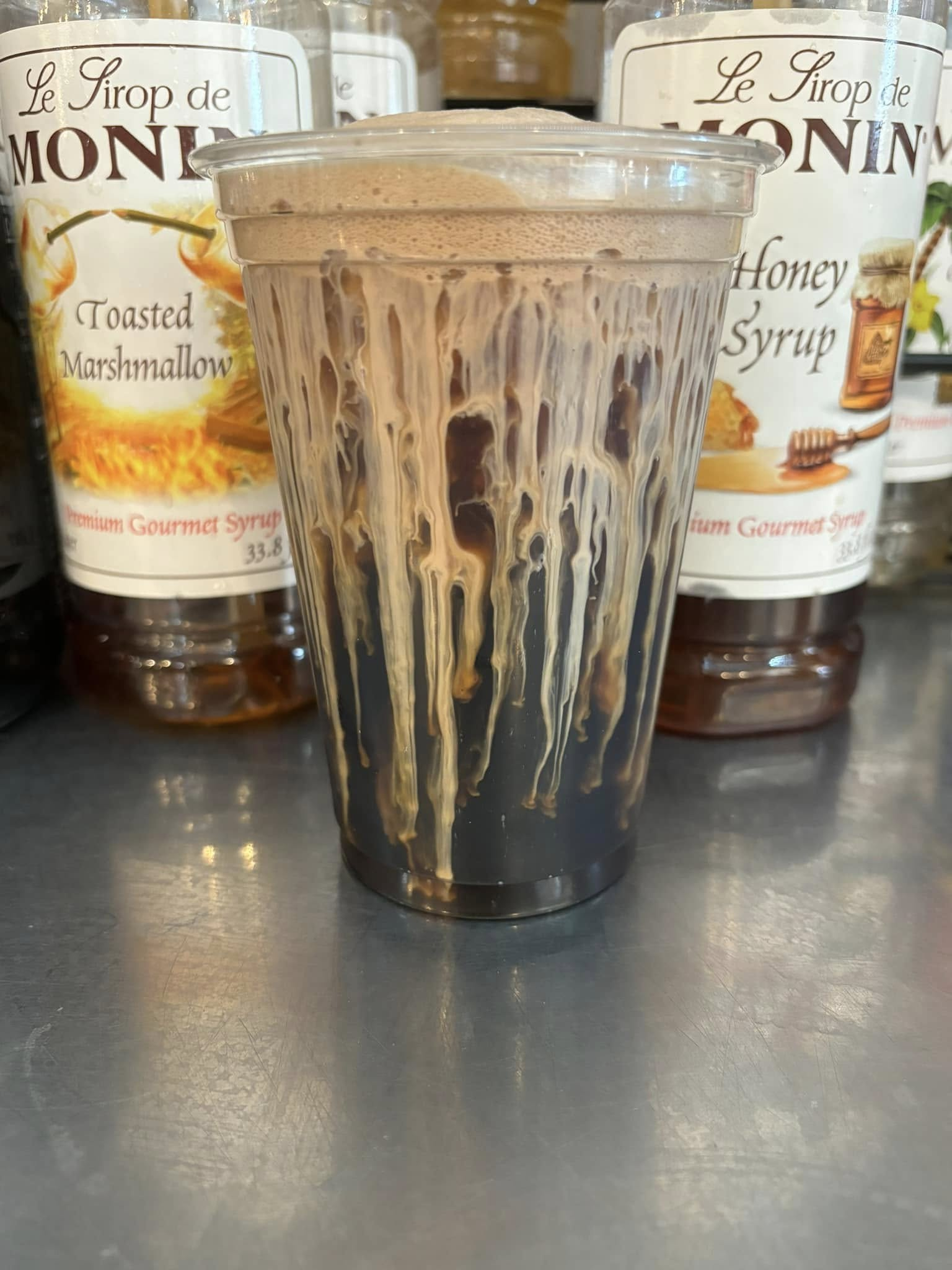 Frosted dark drink in a clear plastic cup with syrup dripping down the sides.