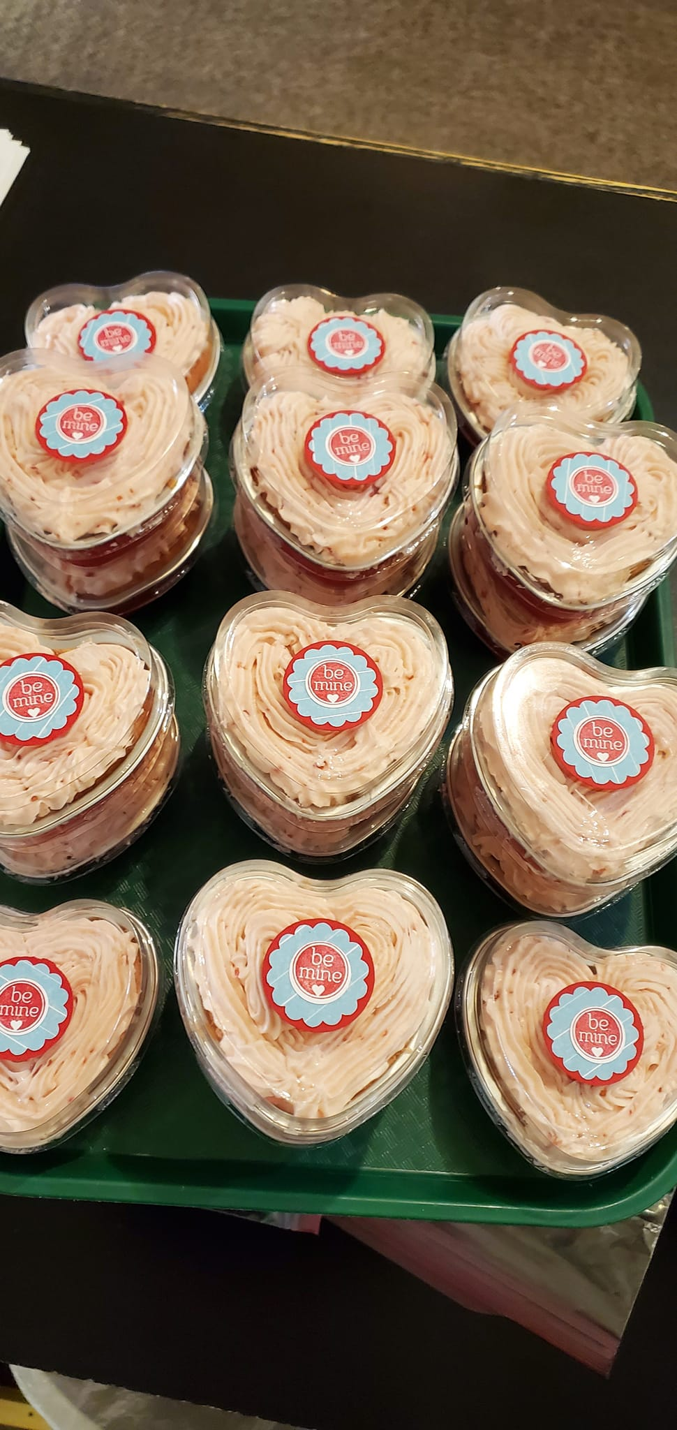 Tray of heart-shaped cakes with a frosted top and a logo in the center.