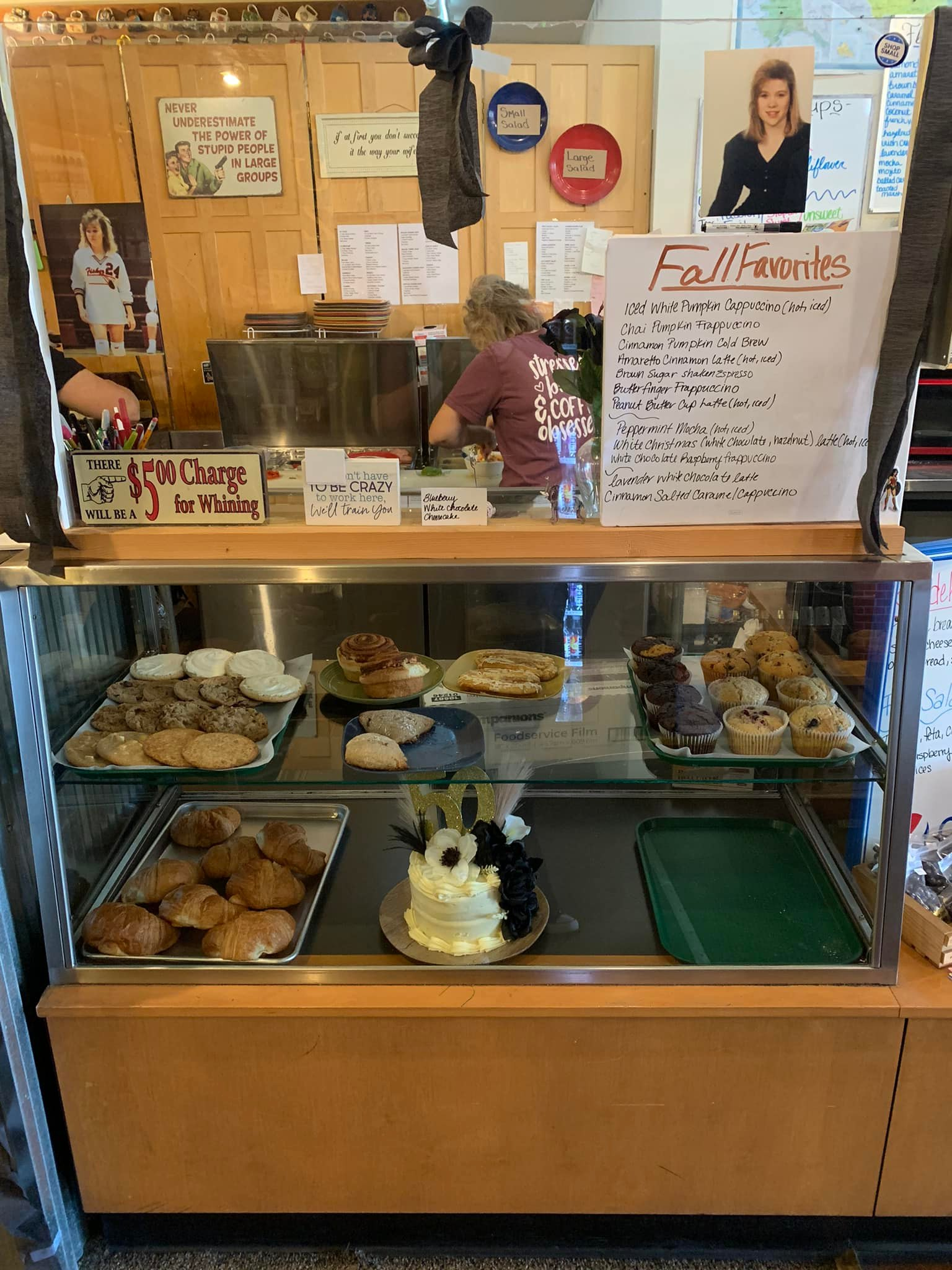 Bakery display case with pastries and a worker behind the counter. A menu board is visible.