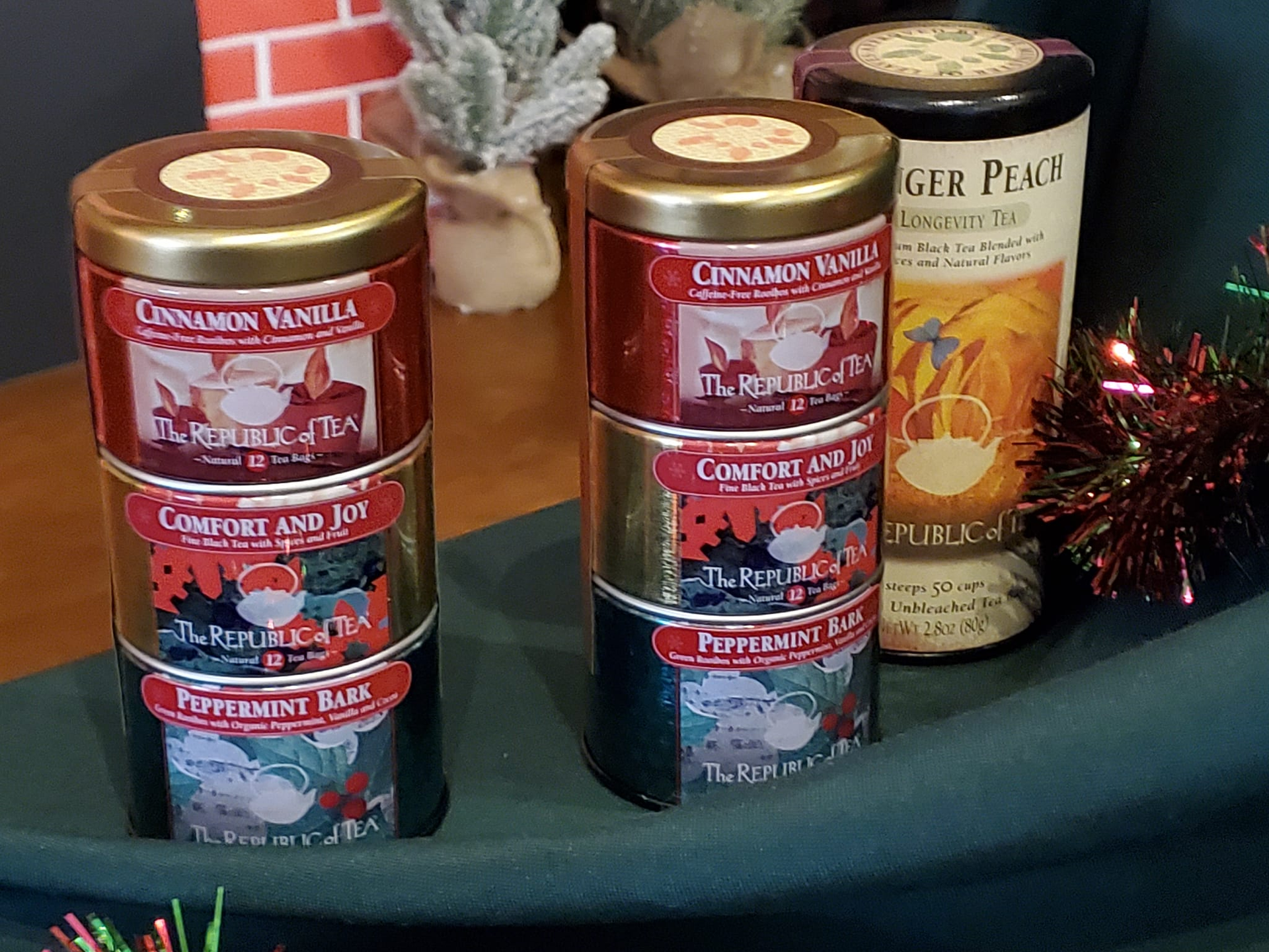 Stacked tea tins: Cinnamon Vanilla, Comfort and Joy, Peppermint Bark, against a festive background with a Ginger Plum tin.