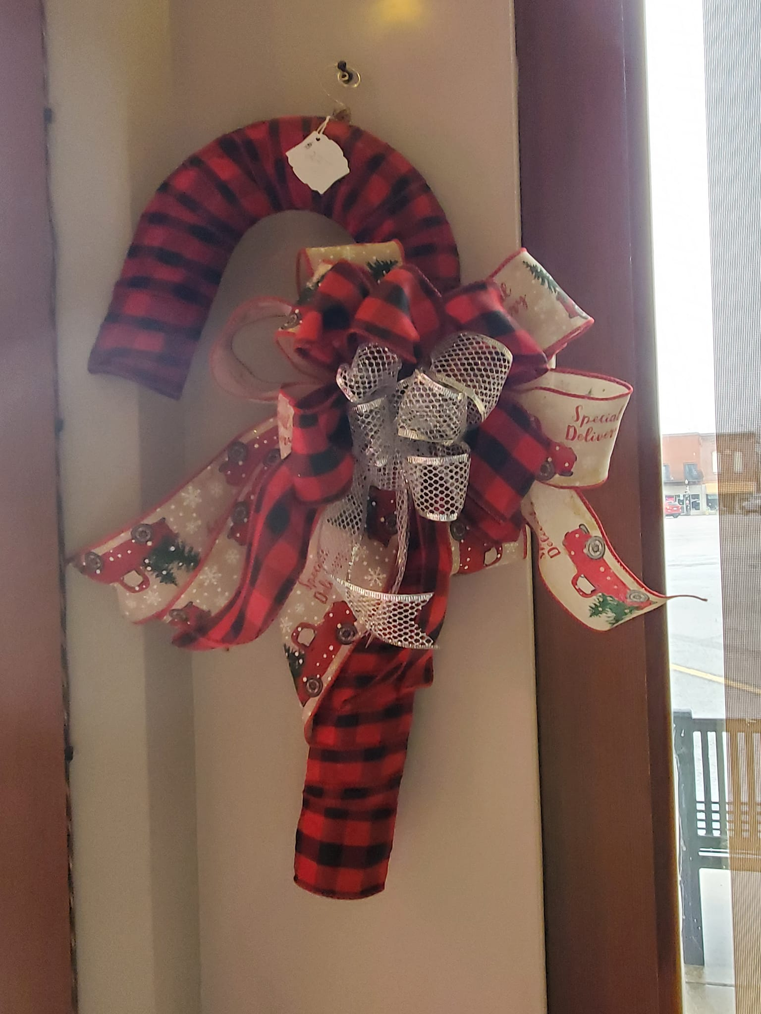 Candy cane decoration with red and black plaid pattern, bow with red, white, and silver ribbons, hanging on a wall.