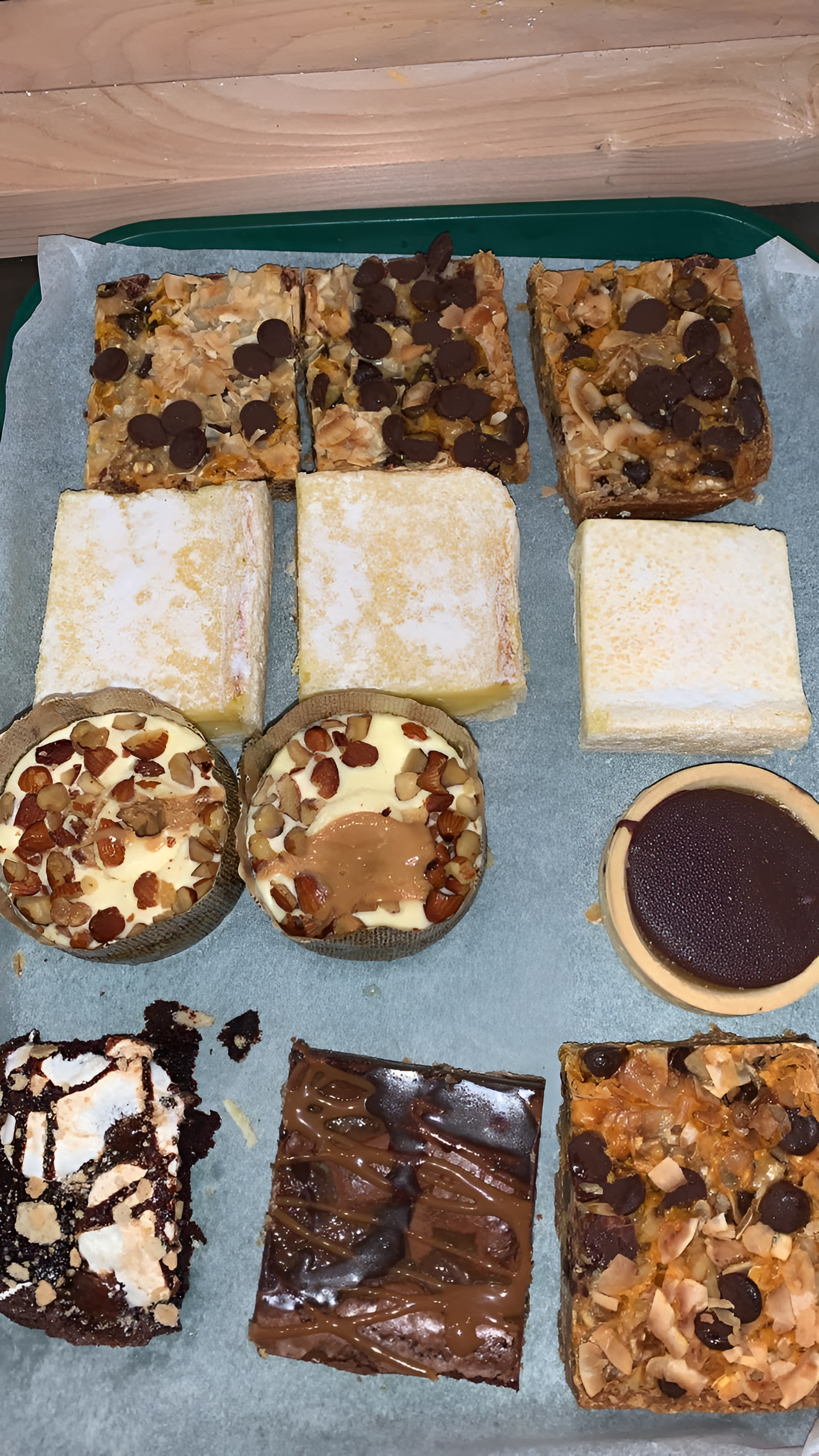 Assortment of baked goods on parchment paper: brownies, bars, cookies, and rounds, with various toppings.