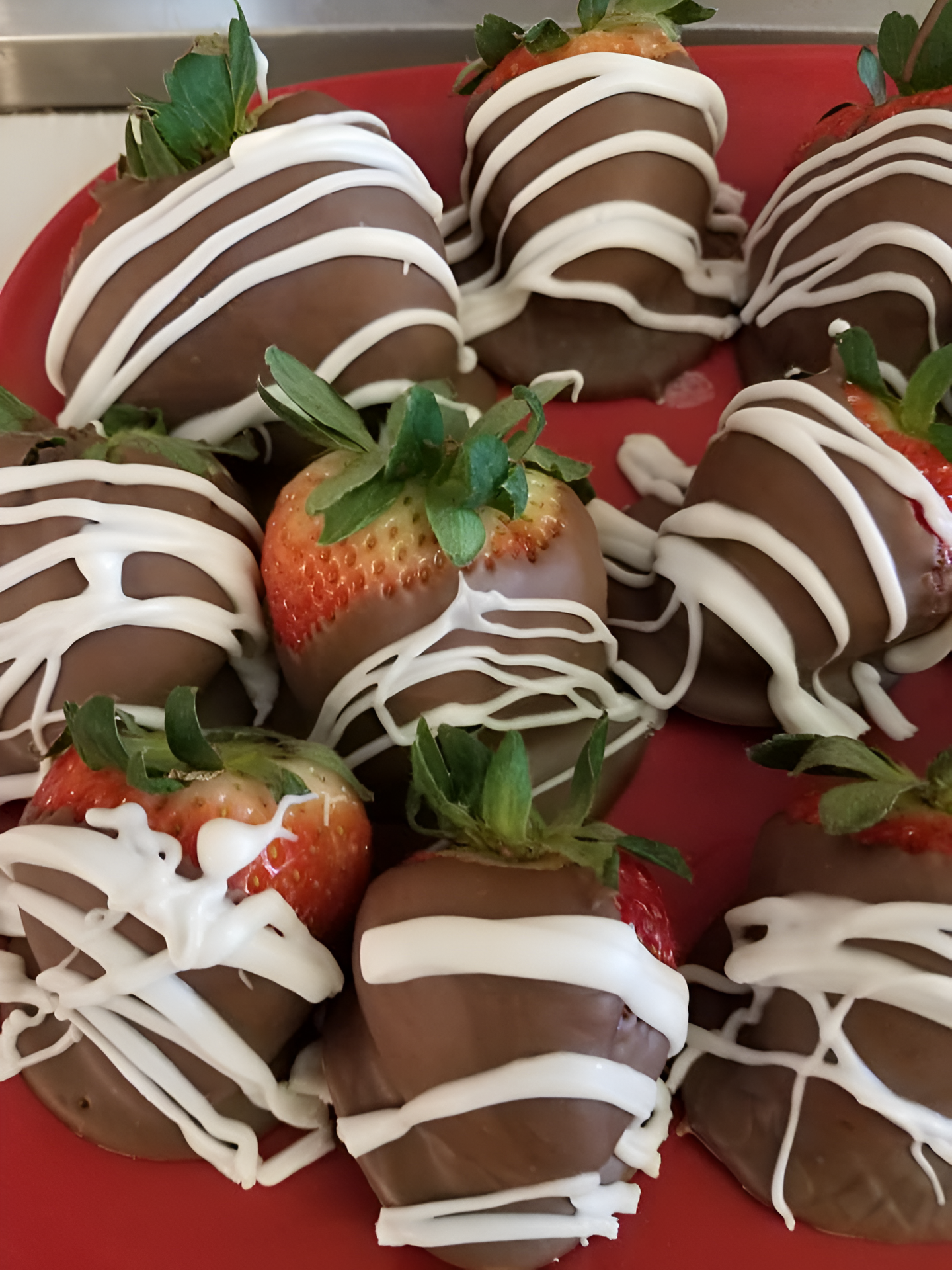 Chocolate-covered strawberries on a red plate. Dark chocolate dipped, drizzled with white chocolate.