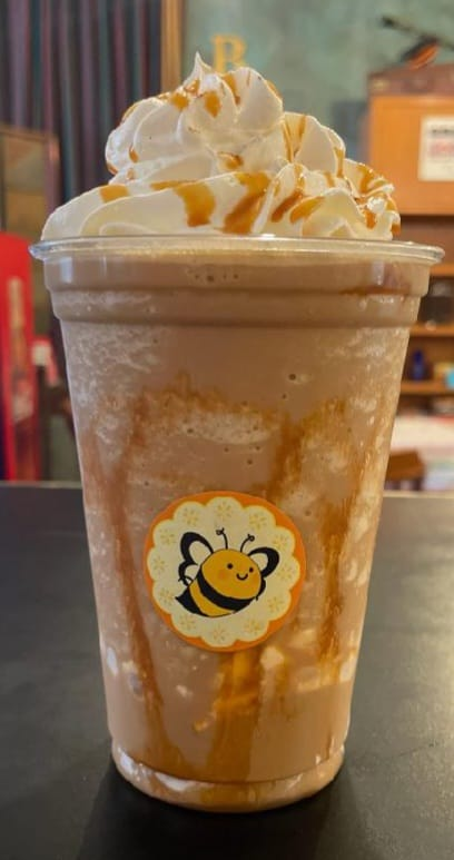 Caramel frappe with whipped cream in a clear cup, logo of a bee on the front.