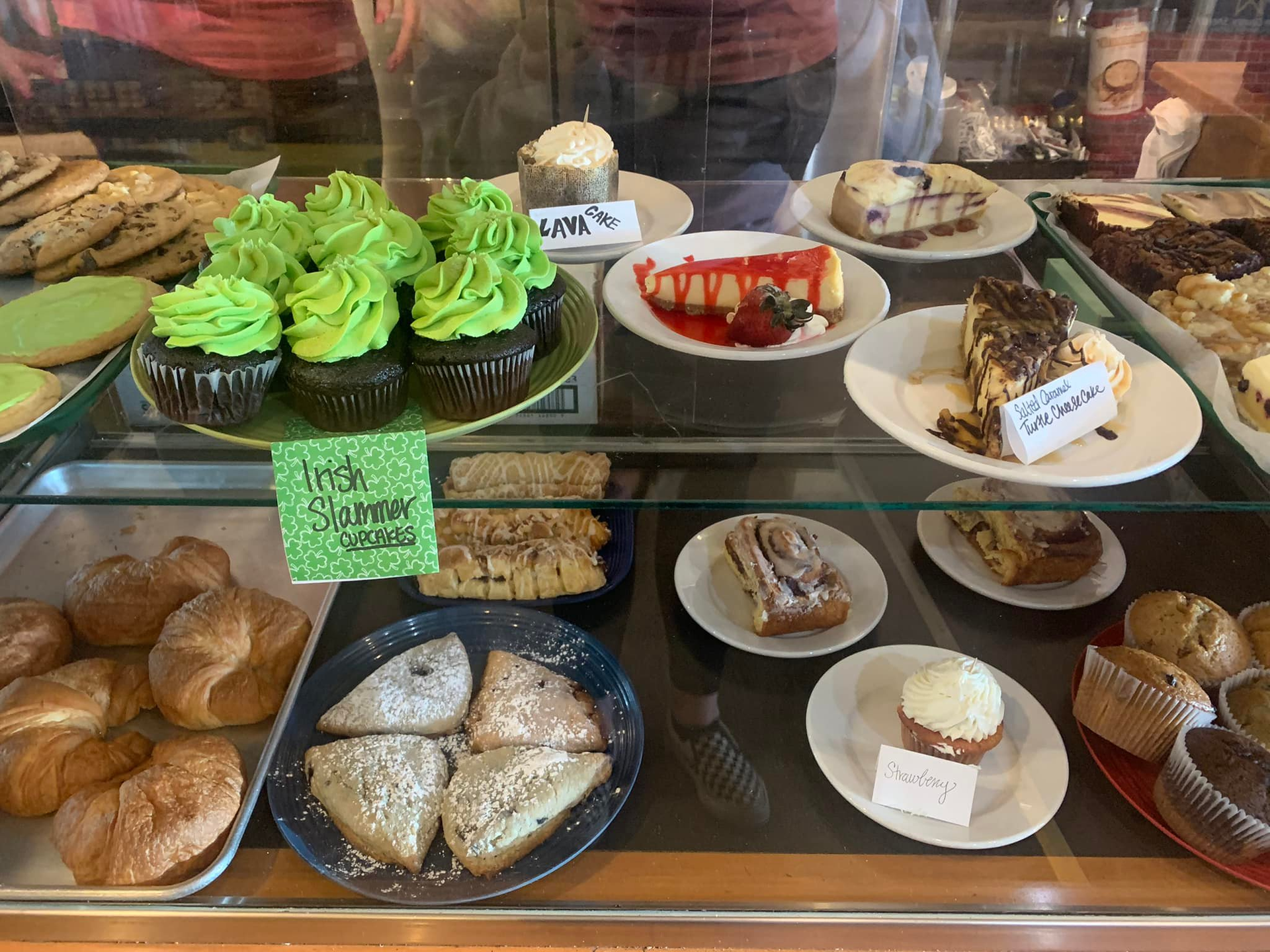 Bakery display case with various pastries: cupcakes, scones, cheesecake, muffins, cookies.