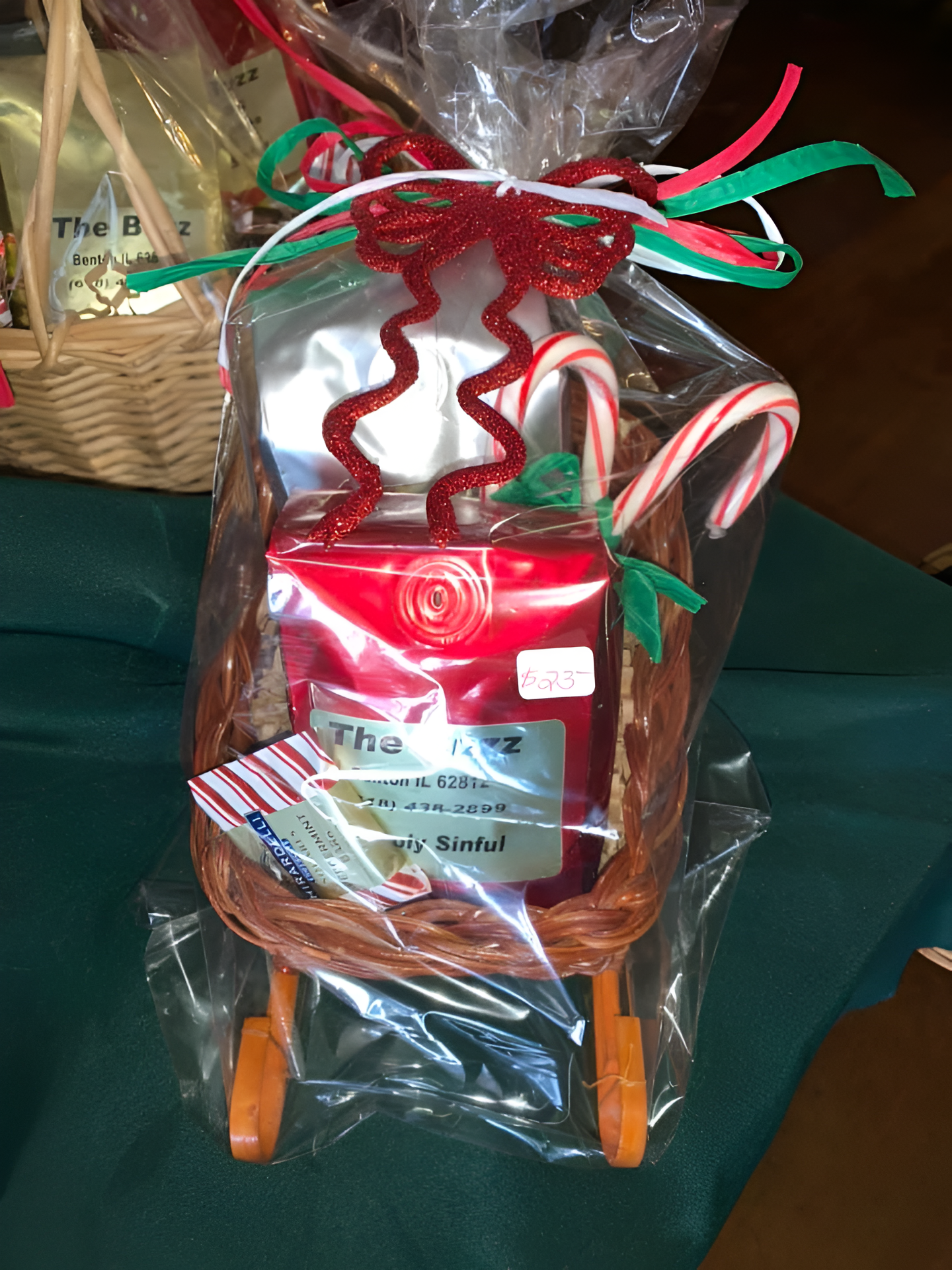 Christmas gift basket shaped like a sleigh, wrapped in cellophane, decorated with candy canes and a glittery red bow.
