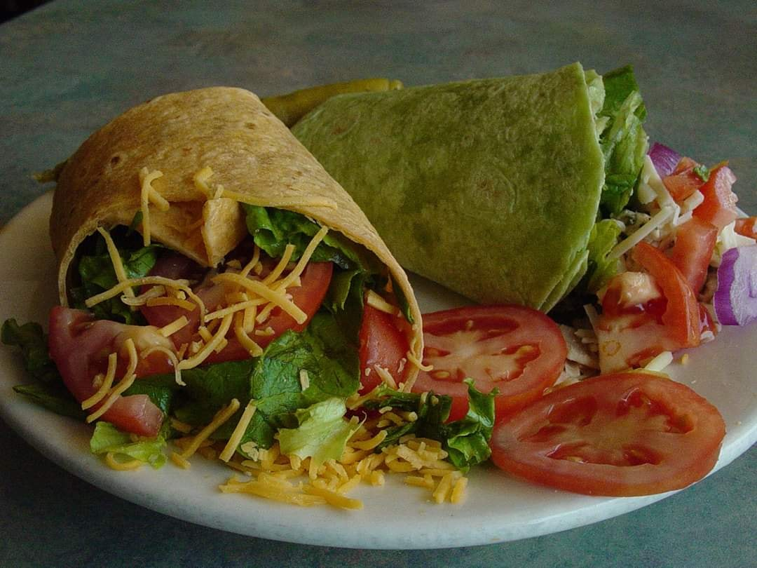Wraps with lettuce, tomato, and cheese on a plate, with sliced tomatoes and a small salad.