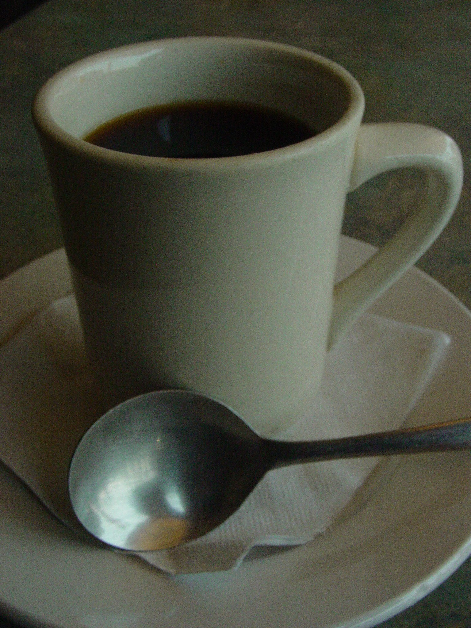A mug of dark coffee on a saucer with a spoon.