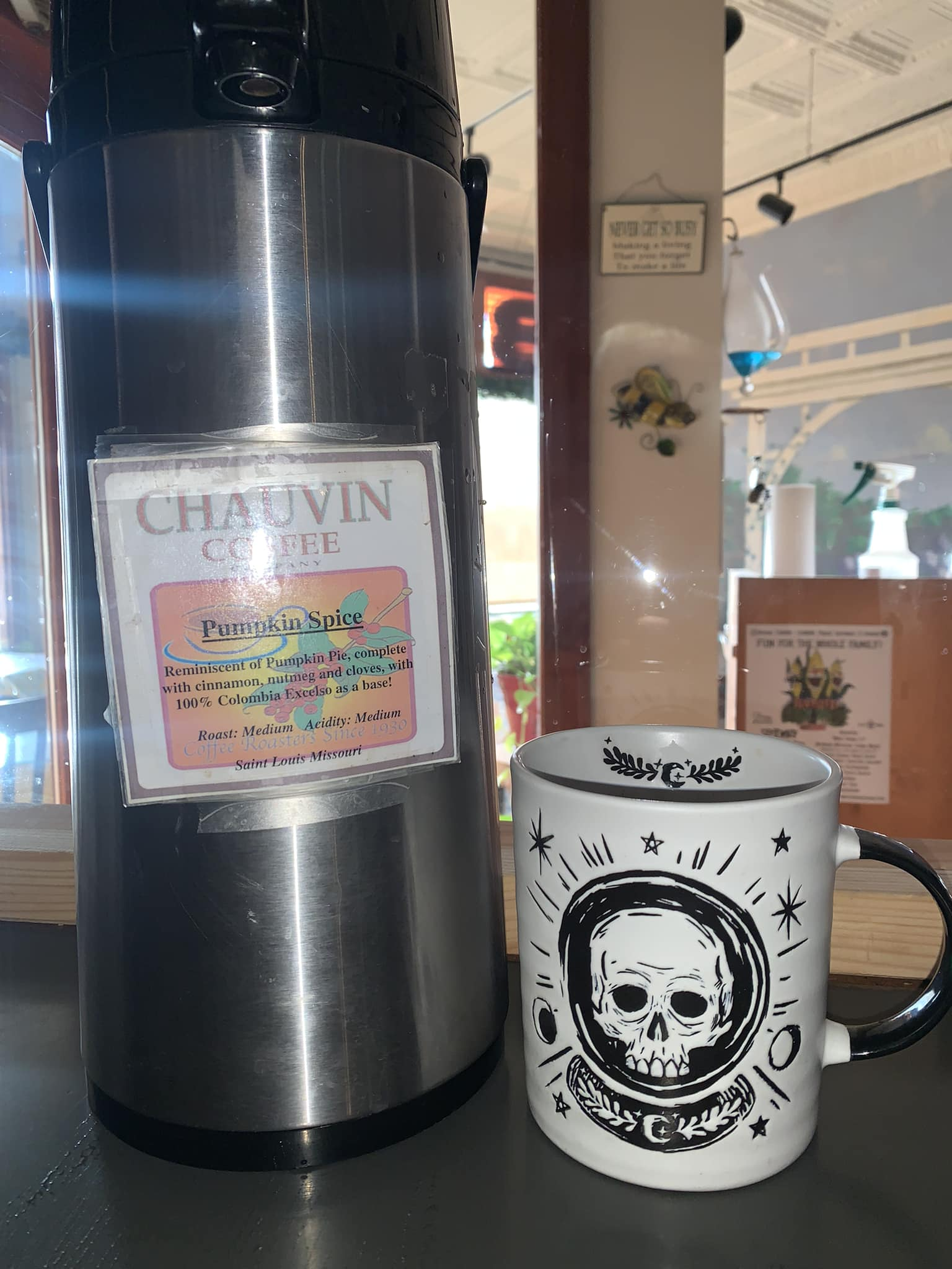 Stainless steel coffee urn and skull mug on a counter, with a sign on the urn that reads “CHAUVIN COFFEE.”