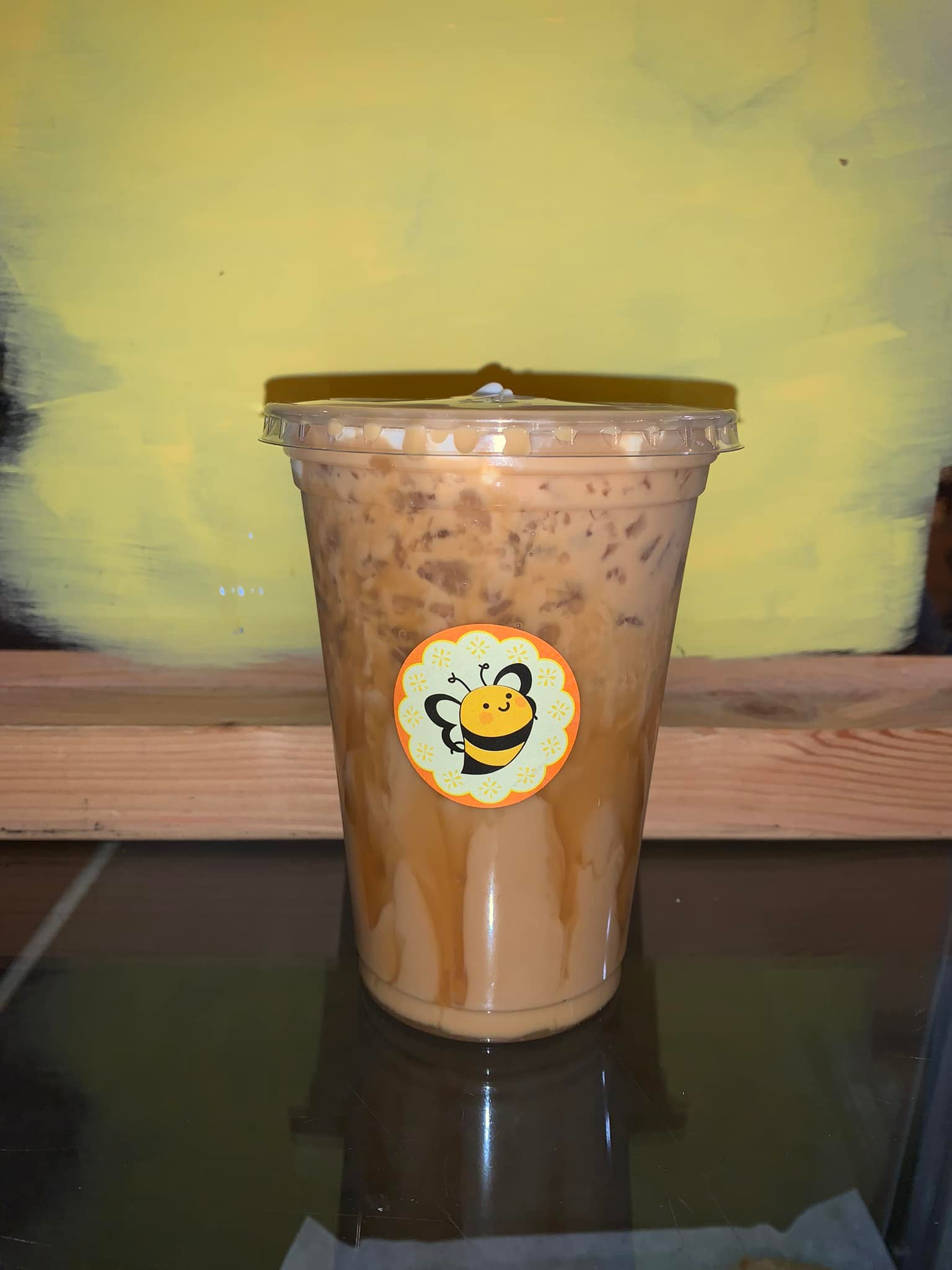 Iced coffee in a clear plastic cup with a bee logo sticker.