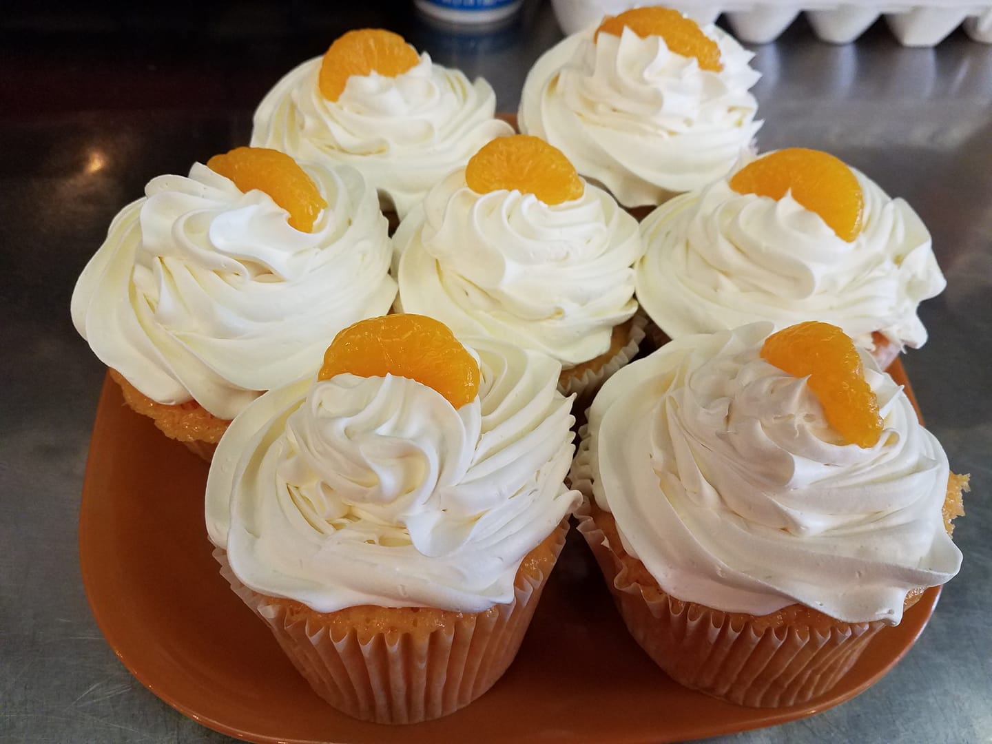 Cupcakes with white frosting and orange segments on a brown plate.