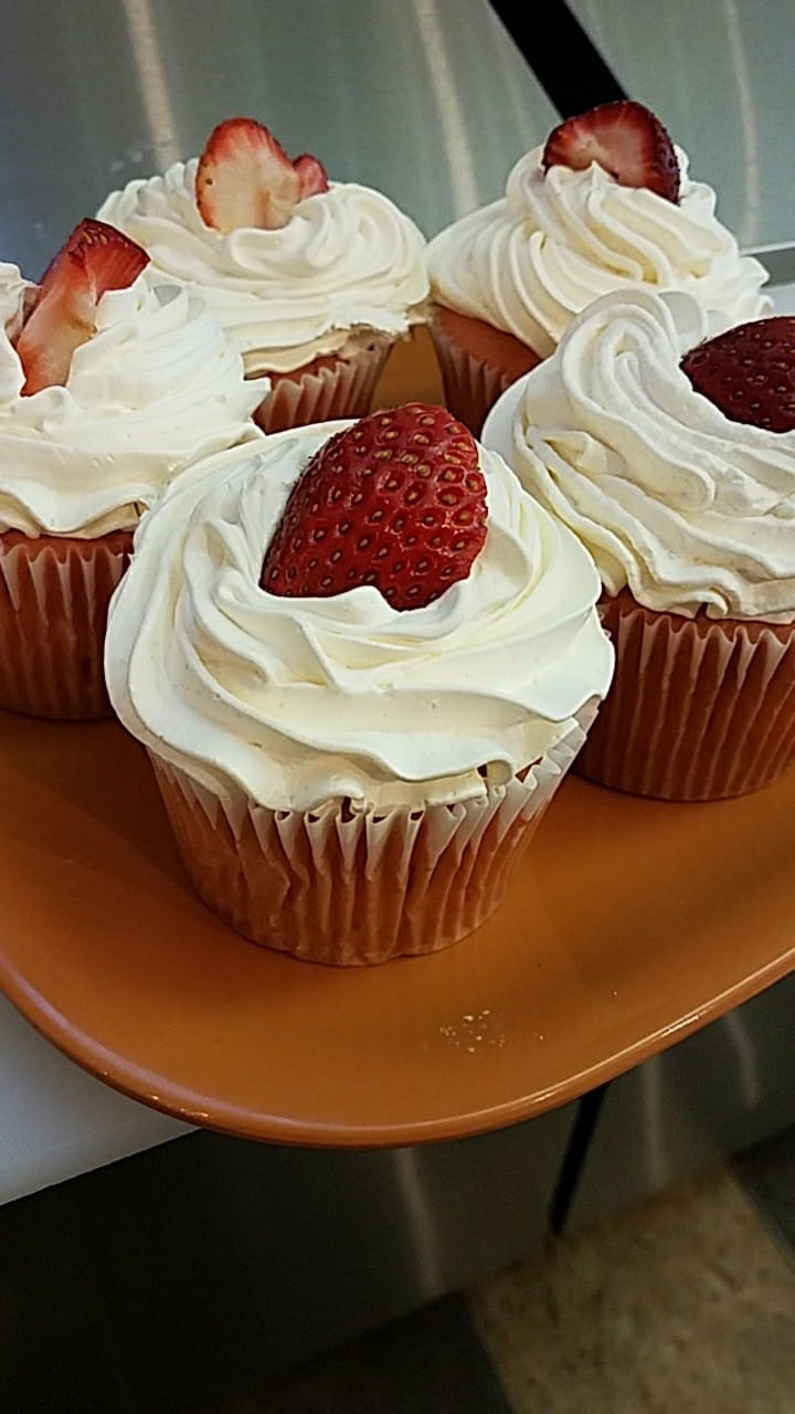 Strawberry cupcakes with white frosting on an orange plate.
