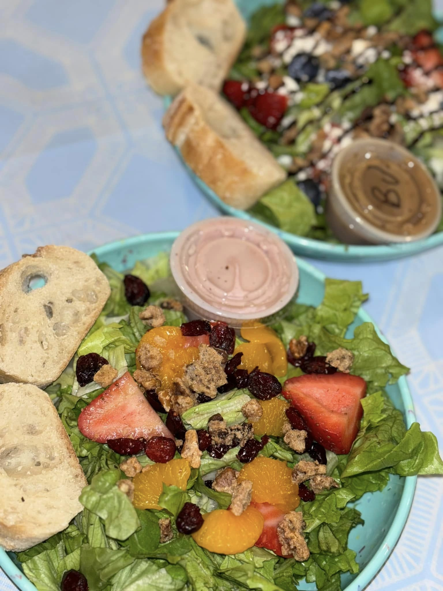 Salads with fruit, granola, and dressing in blue plates, served with bread.