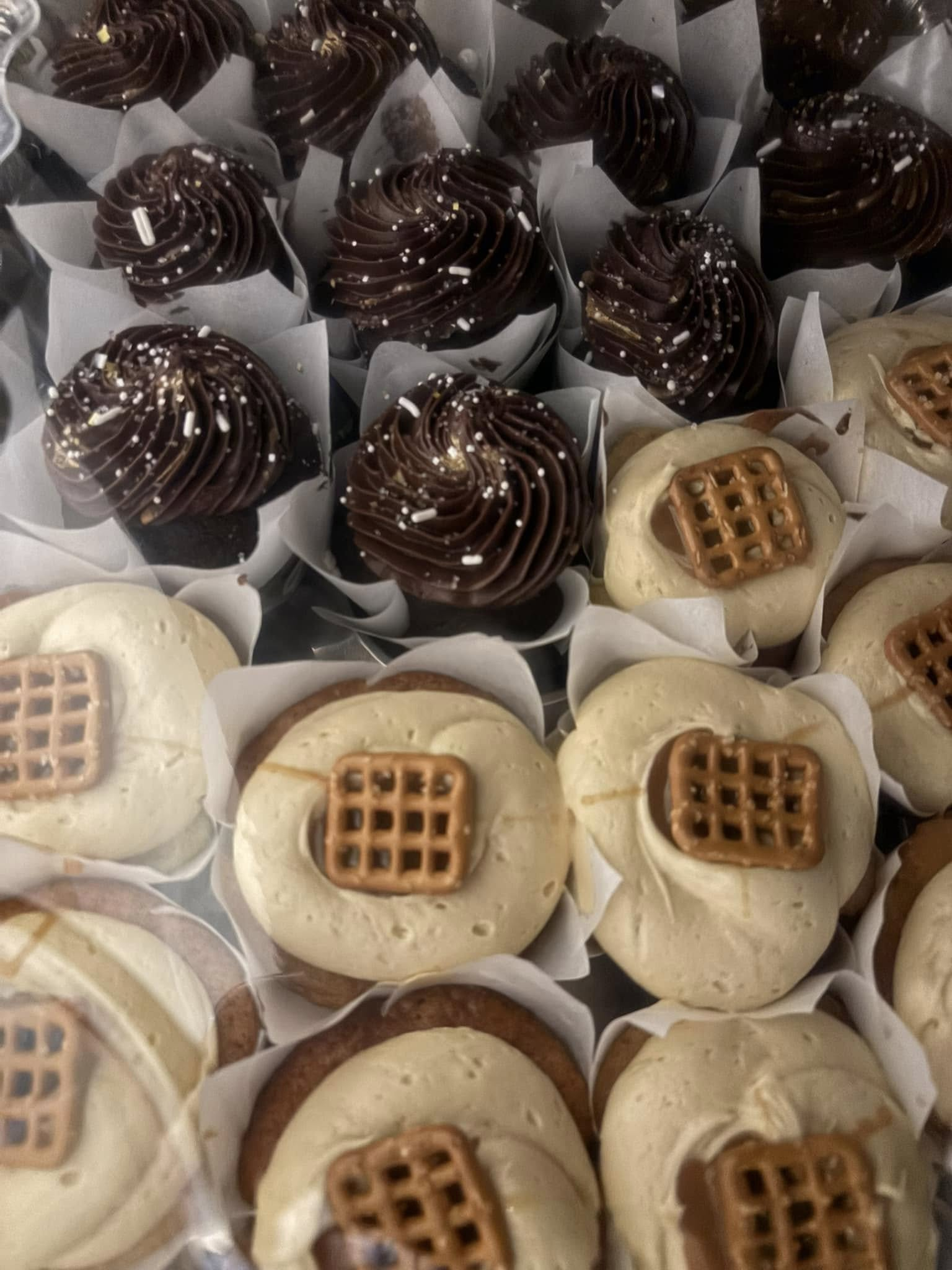 Close-up of cupcakes in paper liners, some with chocolate frosting and sprinkles, others with pretzels.