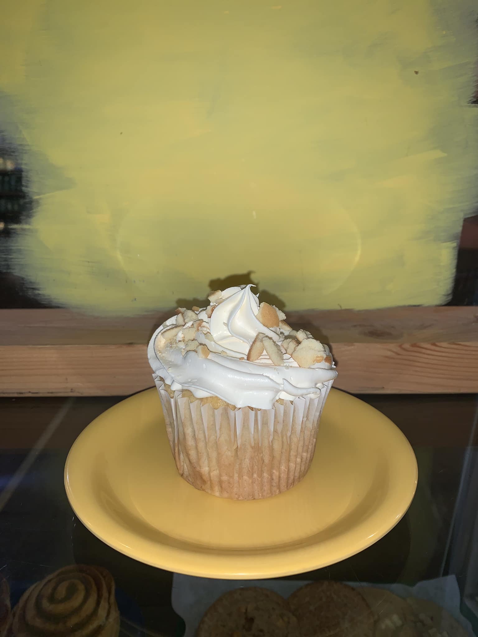 Cupcake with white frosting and nuts on a yellow plate. Yellow background.