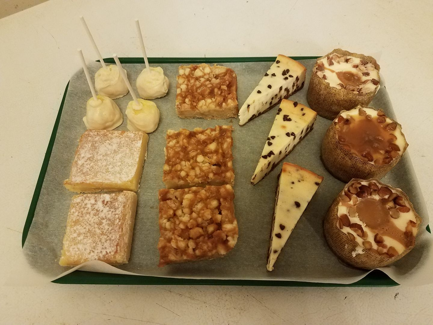 Tray of various desserts: cake pops, squares with toppings, and slices of cheesecake.