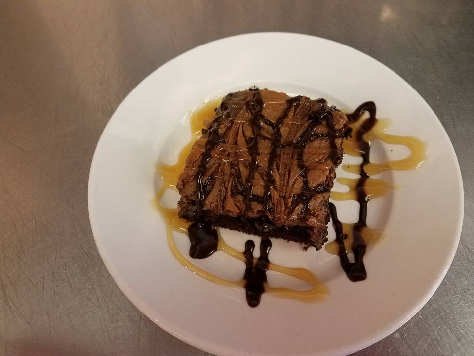 Brownie topped with chocolate and caramel sauce on a white plate.