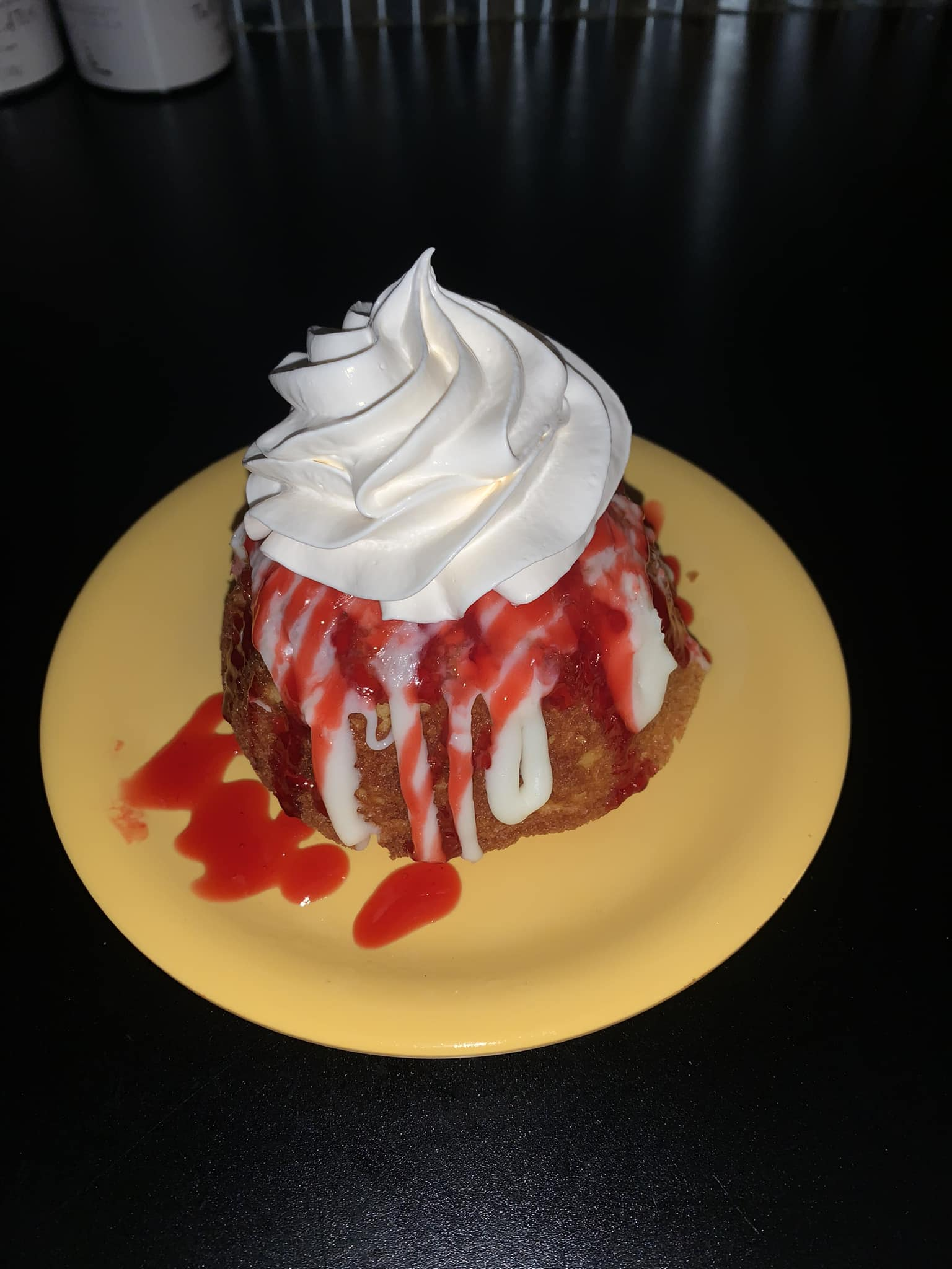 Dessert with whipped cream, strawberry drizzle, on a yellow plate, black background.