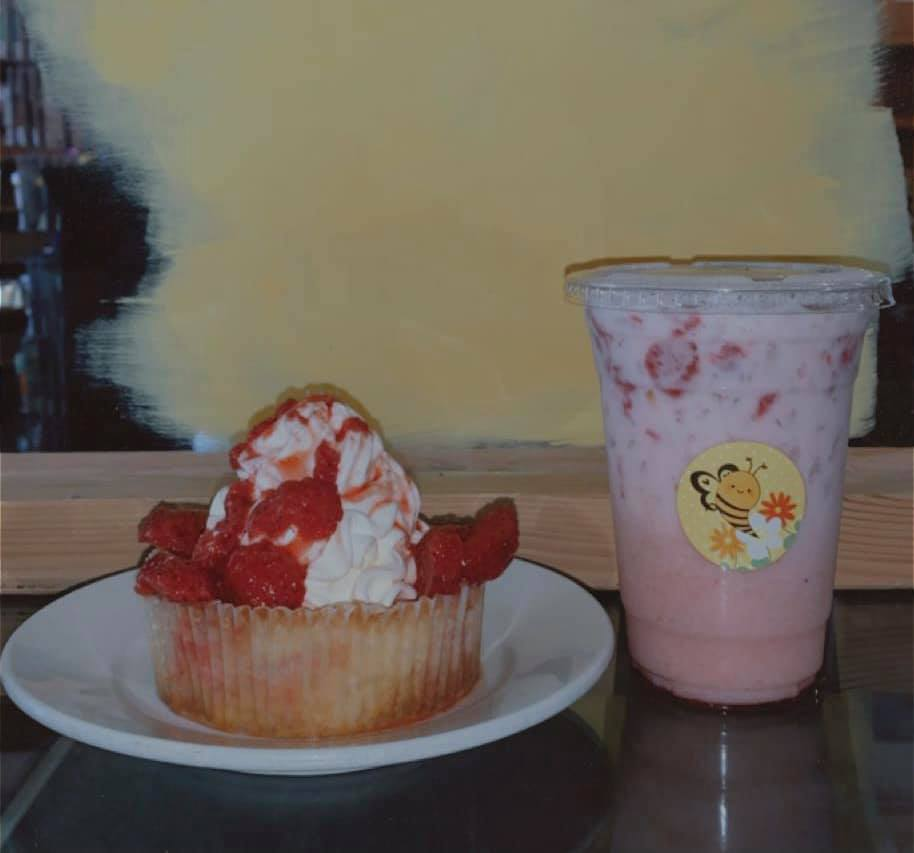 Strawberry cupcake and pink drink with bee sticker on a counter.