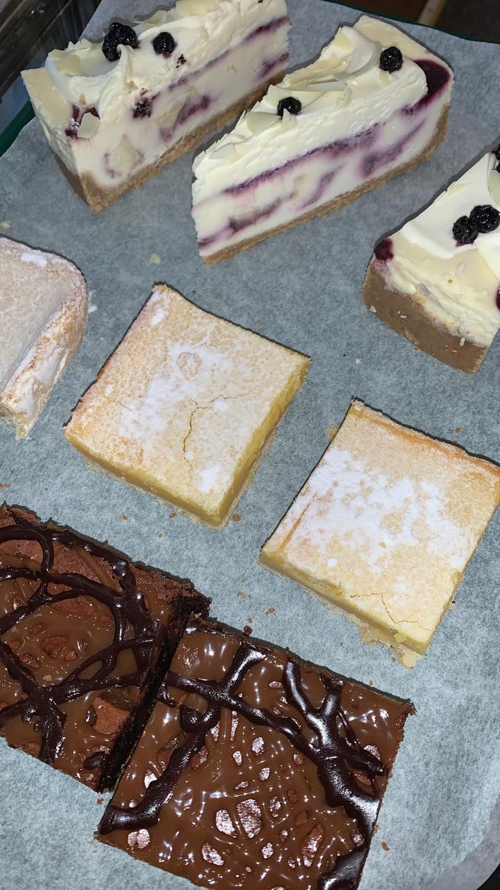 Assorted baked goods: cheesecake slices, blondies with powdered sugar, and chocolate brownies drizzled with chocolate.