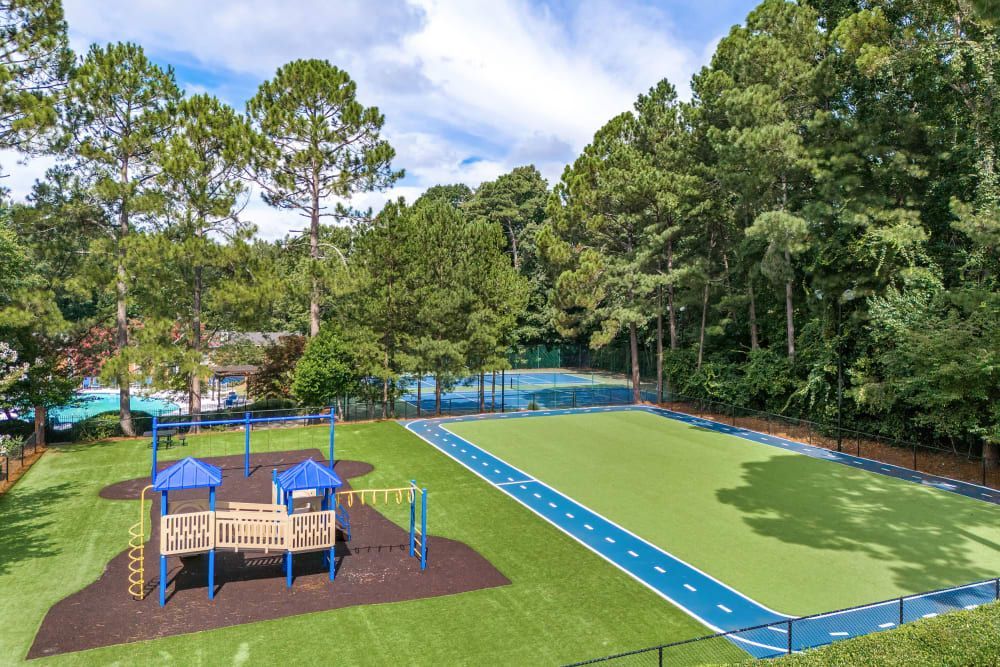 An aerial view of a playground, tennis court, and blue walking track surrounded by trees at Marquis at Perimeter Center in Atlanta, GA.