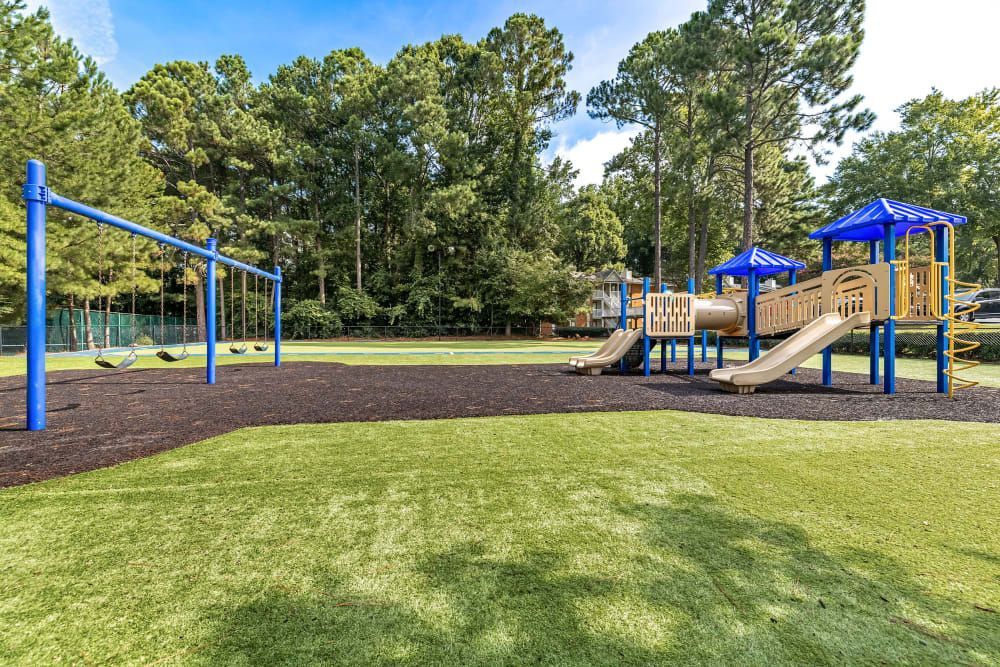 A playground with a slide, swings, and a tunnel with trees in the background at Marquis at Perimeter Center in Atlanta, GA.