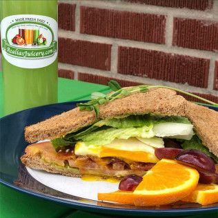 Sandwich on a plate with fruit slices and a green drink on a table