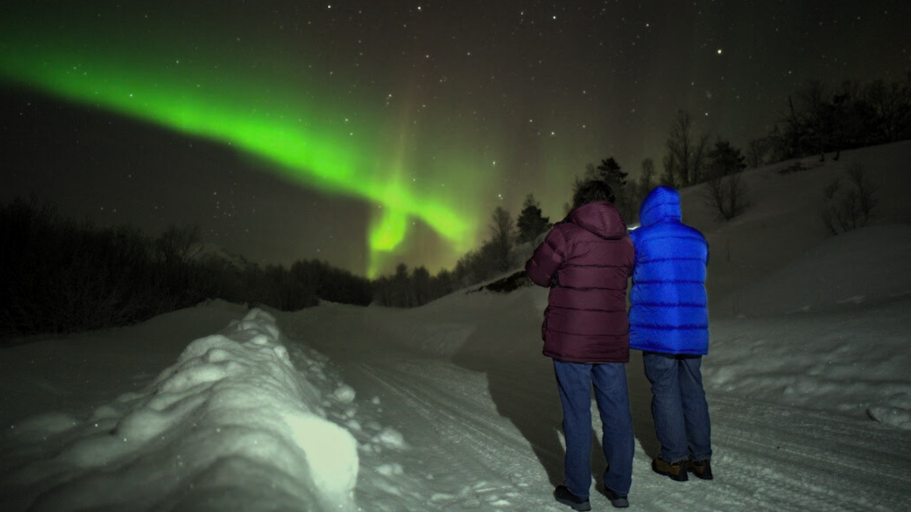Two couples dressed in winter clothing standing infront of aurora northern lights scene in tromso Norway