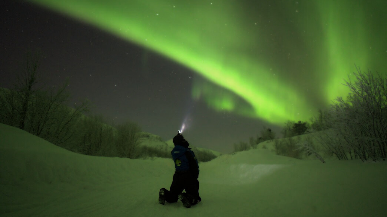 aurora guide holding a head light aiming to the sky and the sky is covered with aurora colors