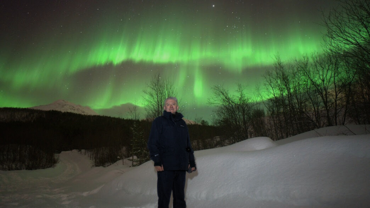 man standing infront of aurora northern lights background and dreed in winter clothing