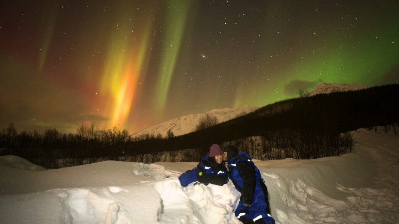two couples kissing under the sky colored in red and green northern light color in tromso northern light tours