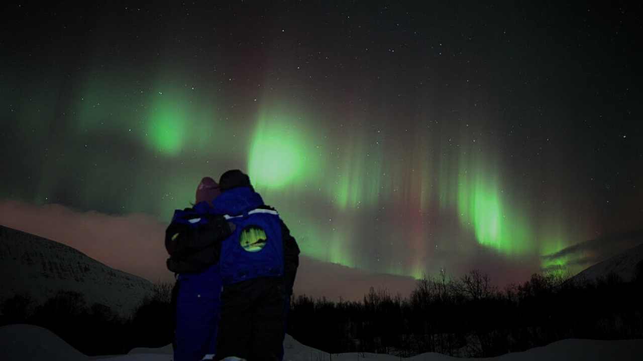 couples standing infront of mesmerizing northern light sky in tromso norway