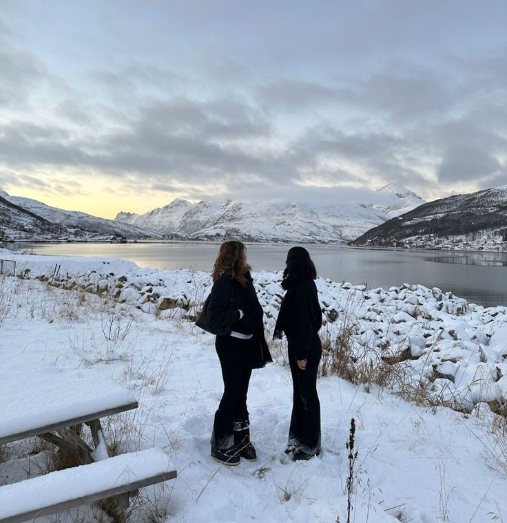 two girls standing by the sea dressed in winter clothing and the weather is cloudy