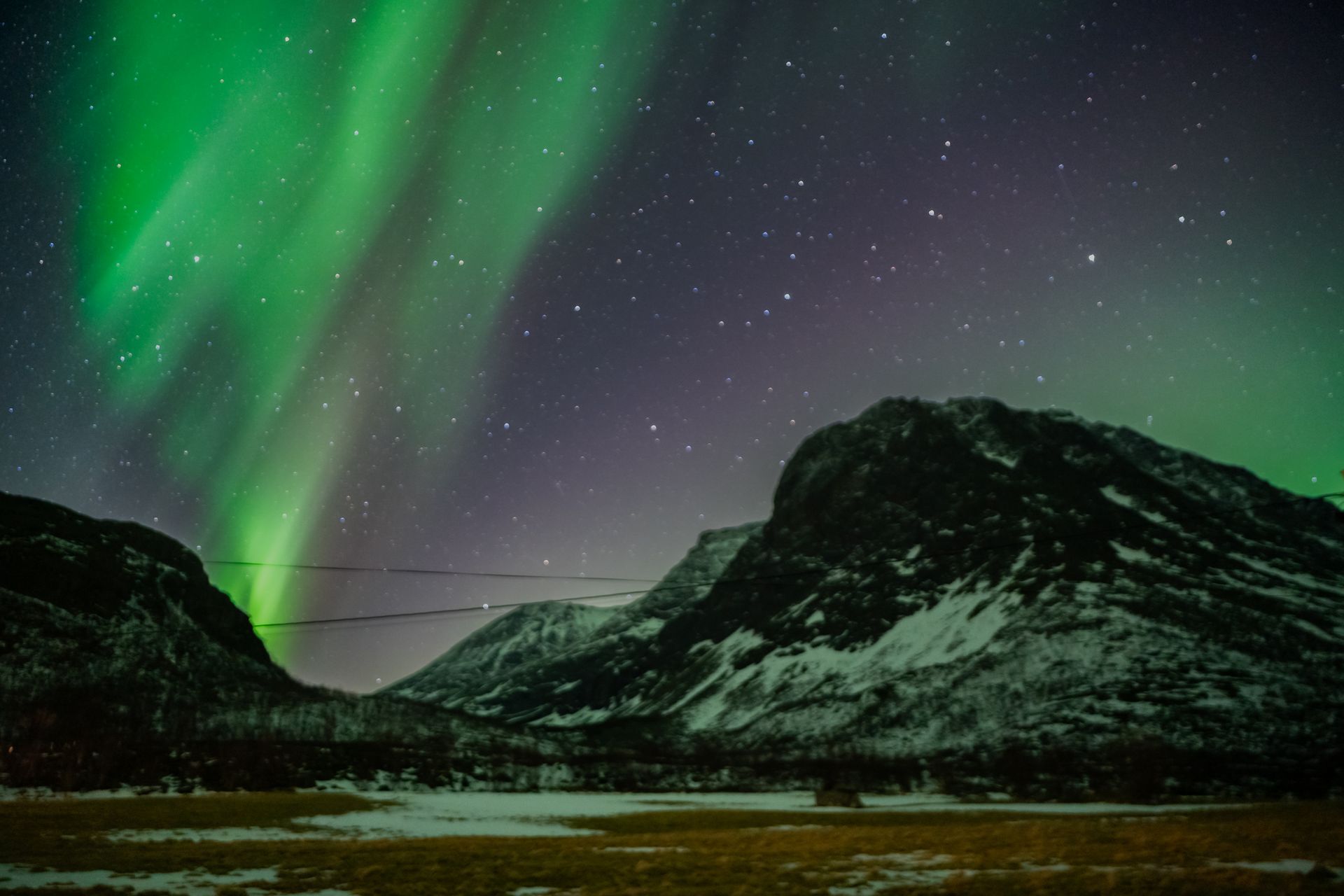 Green Northern Lights over snow-covered Arctic mountains in Tromsø, photographed under real conditions without edits