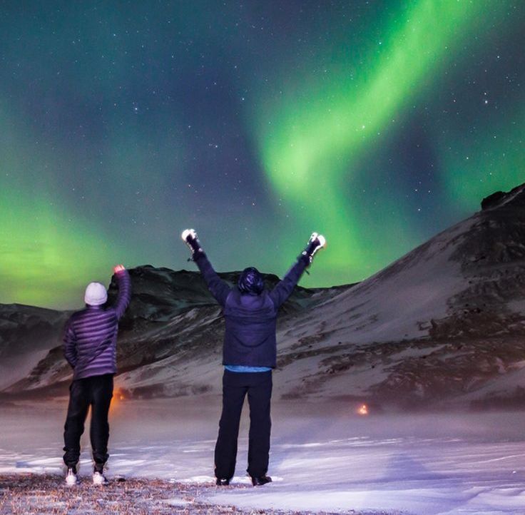 two men rising hand under northern light sky in tromso norway