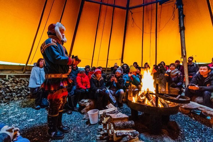 Tromso reindeer camp tent and sami man standing infront of some travelers sitting and listening to joyk all dressed in winter clothing