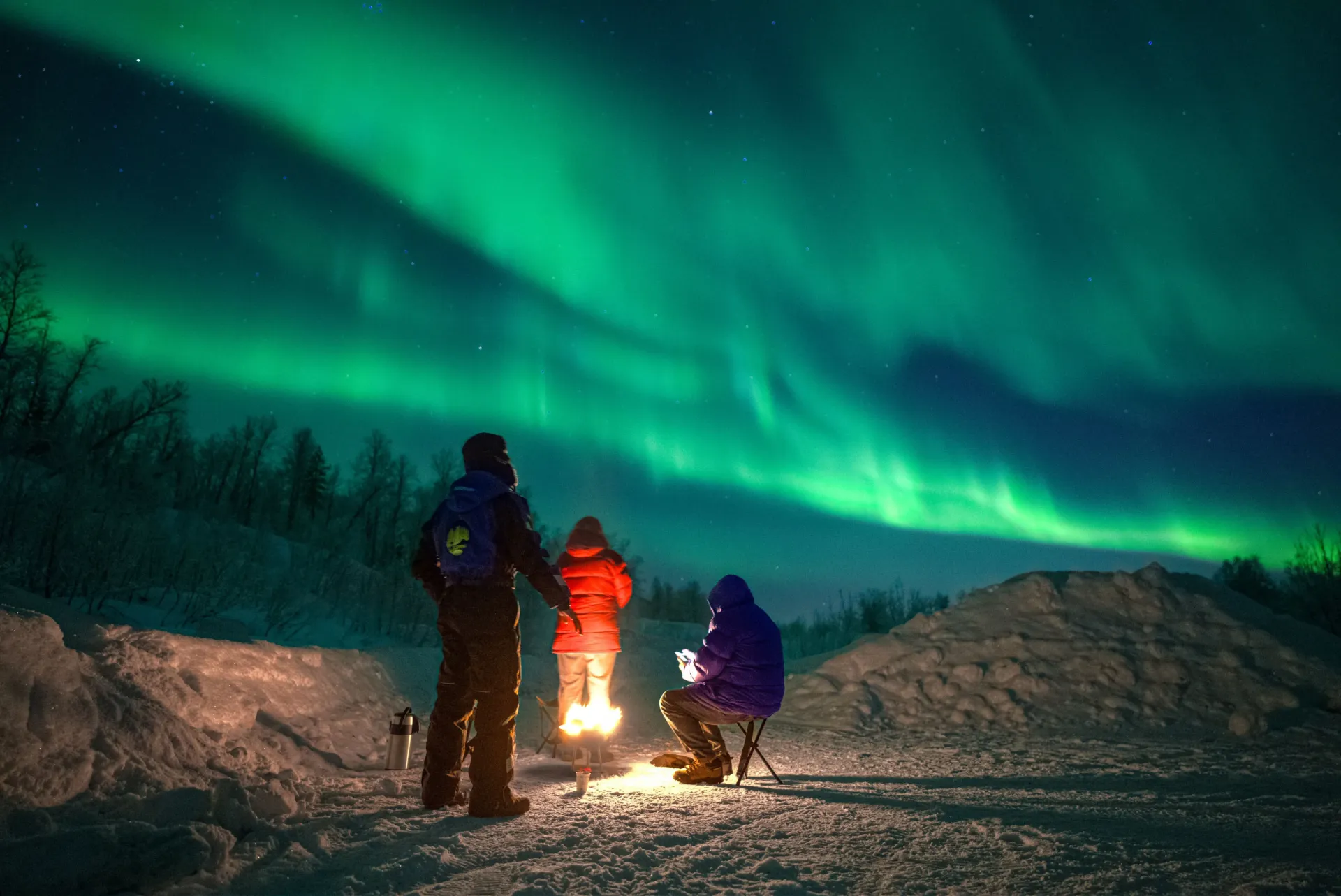Guest sitting in snow watching Northern Lights Tromsø small group aurora tour winter Norway