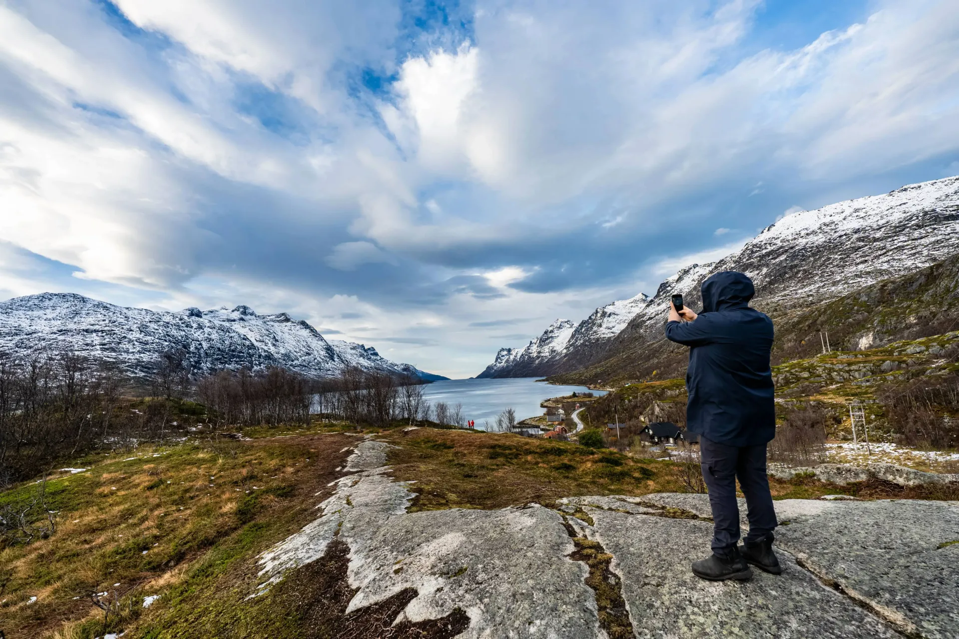 Traveler taking a photo of an Arctic fjord and snow-capped mountains in Northern Norway